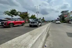 1. Mobil sedan di jalan utama Bukamata.id, lalu lintas lancar di area perkotaan.